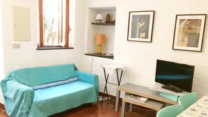 A room with a teal sofa, a television, a small table, and a window with a view of the outside. - Ca du Paraxo (Levanto)