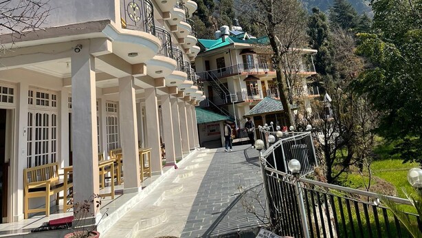 A multi-story building with balconies, a staircase leading to the entrance, and a view of mountains in the background. - Hotel Sky pie (Dharamshala)
