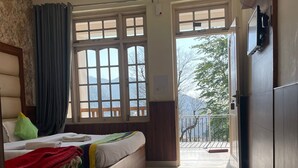 A hotel room with two beds, a ceiling fan, large windows, and a view of the outdoors. - Hotel Sky pie (Dharamshala)