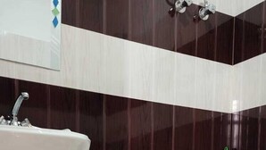A bathroom with a pedestal sink, a toilet, and a bidet. The walls have a striped tile pattern. - Hotel Sky pie (Dharamshala)
