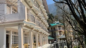 A multi-story hotel with balconies, a covered outdoor seating area, and a mountainous backdrop. - Hotel Sky pie (Dharamshala)