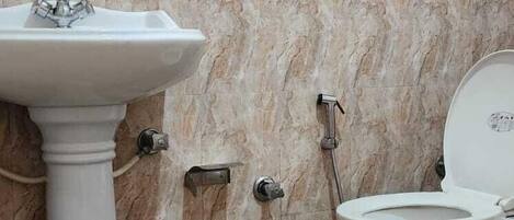 Un baño con pared de mármol, lavamanos pedestal, inodoro y ducha con cabezal de ducha manual.