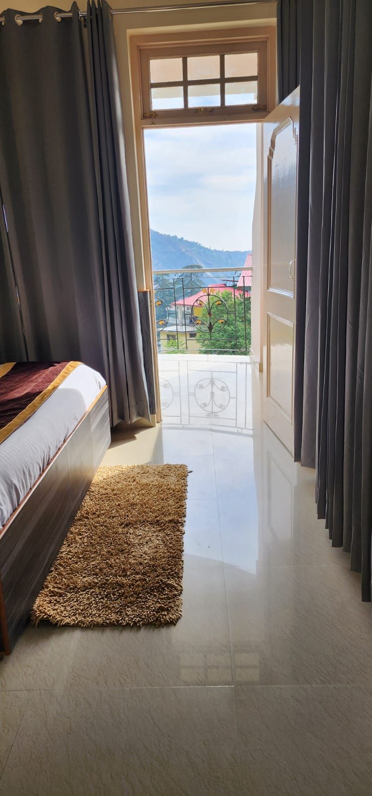 A bedroom with a bed, a window, and a view of a balcony with a railing.