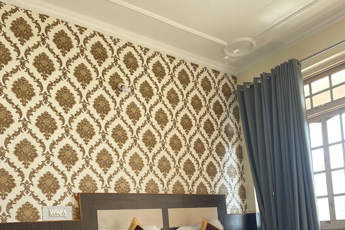 A hotel room with a large bed, a nightstand, a chair, and a patterned wallpaper.