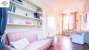 Ein Wohnzimmer mit einem rosafarbenen Sofa, einem weißen Sessel und einem Bücherregal voller Bücher.