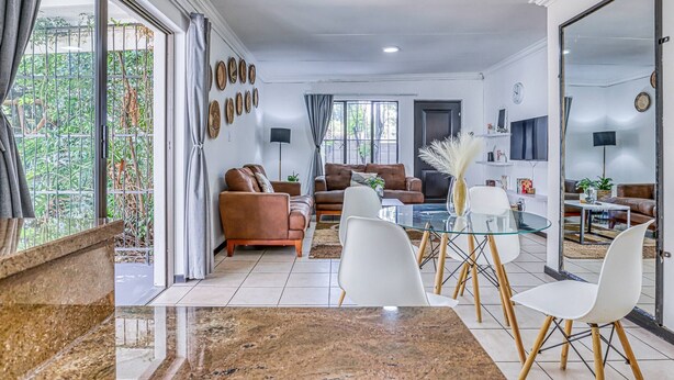 A spacious living area with a glass dining table, two sofas, and a coffee table. - The Cottage-1 Bed-pool-bbq-fibre-solar-samrand (Centurion)