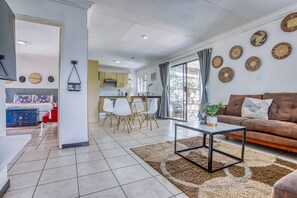 A modern living room with a brown sofa, a coffee table, and a dining area with white chairs.
