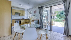 A modern kitchen with a dining area, large windows, and a view of the outdoors. - The Cottage-1 Bed-pool-bbq-fibre-solar-samrand (Centurion)