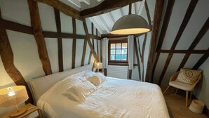 Une chambre avec un grand lit, une table de chevet, une lampe, une fenêtre et une chaise.