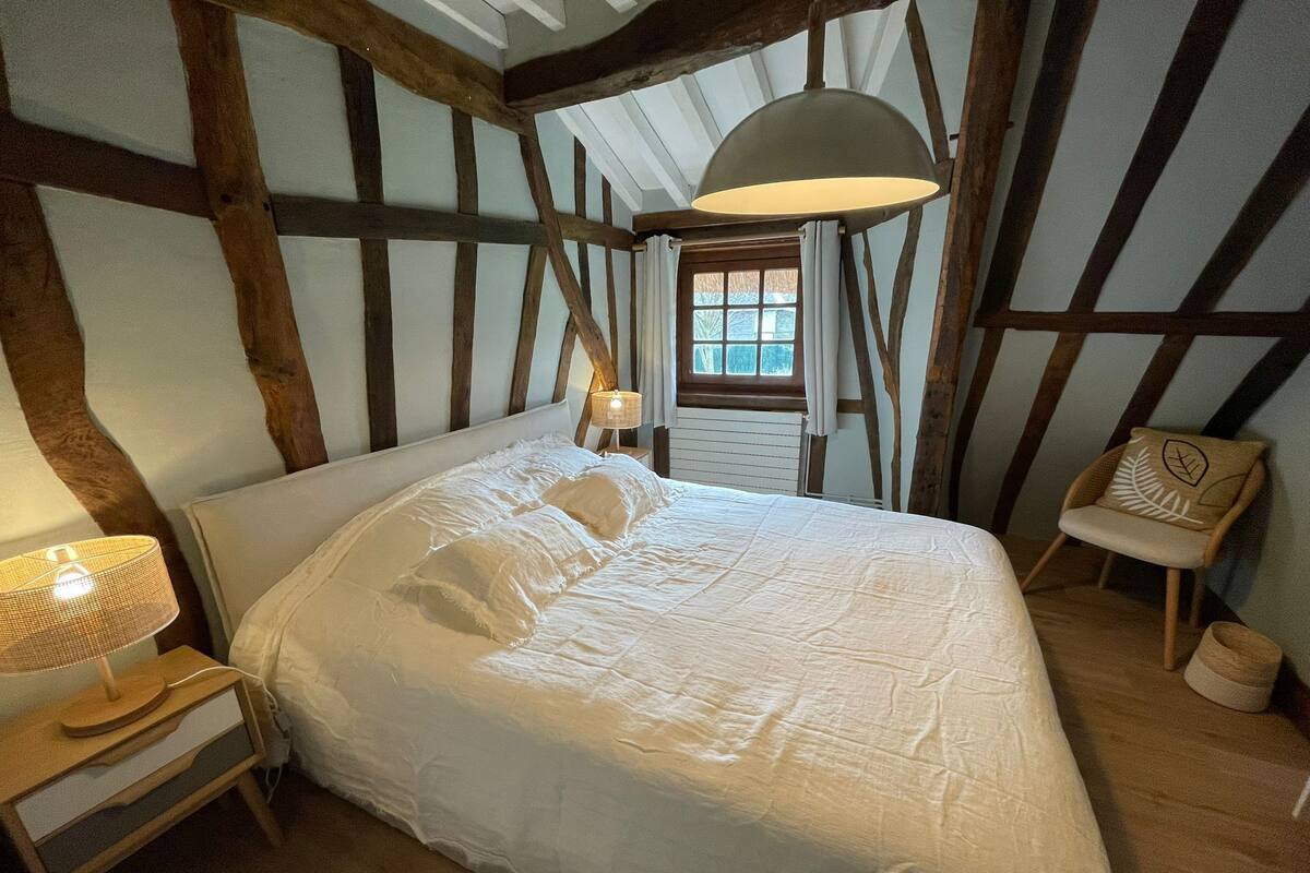 Un dormitorio con una cama grande, una mesita de noche, una lámpara, una ventana y una silla.