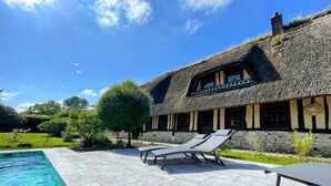 Un bâtiment à toit de chaume, doté d’une façade en pierre, d’une piscine et de chaises longues.