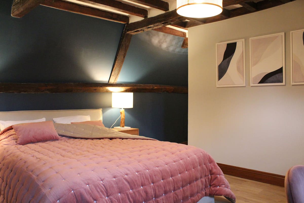 Un dormitorio con una cama grande, vigas de madera, una mesita de noche con lámpara y arte abstracto en la pared.