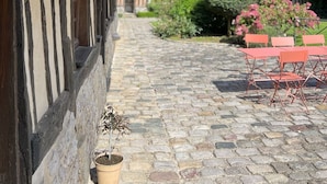 Un bâtiment traditionnel avec un toit de chaume, une horloge bien visible et un chemin pavé menant à un espace extérieur aménagé pour s’asseoir.