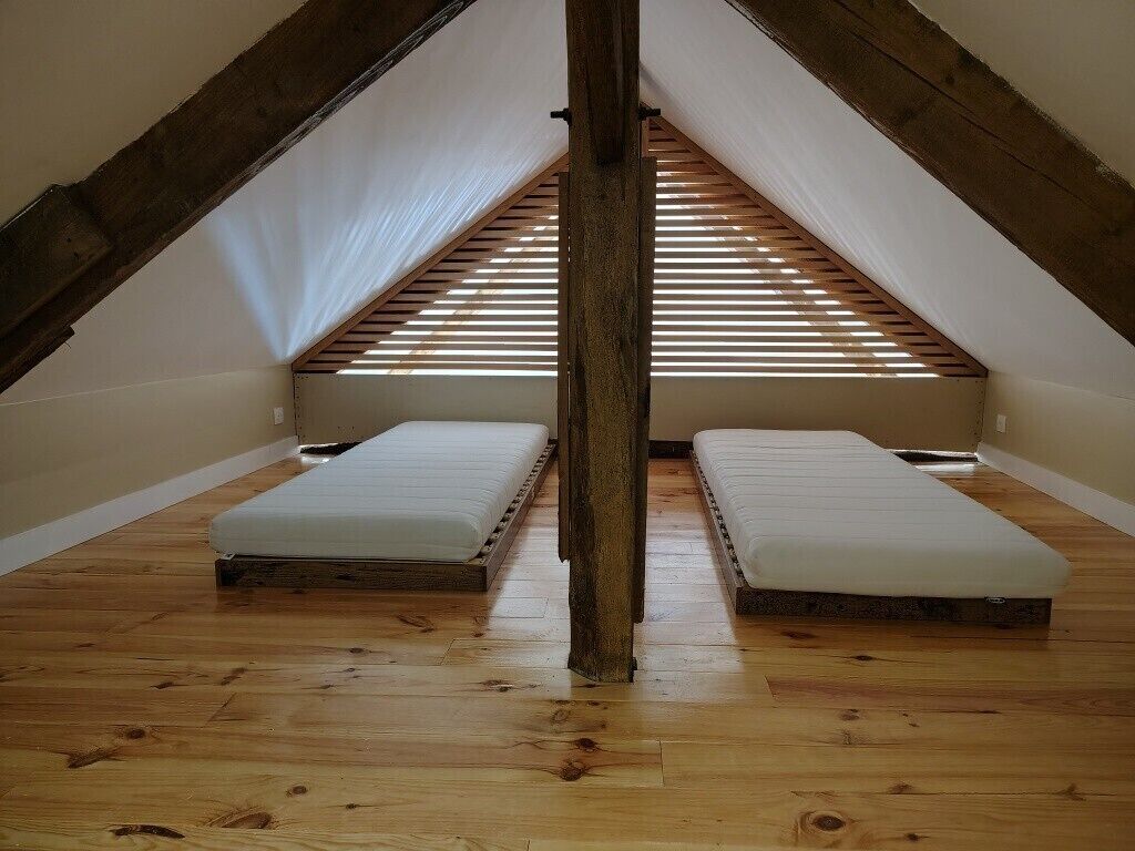 A small attic room with two mattresses, wooden beams, and a sloped ceiling.