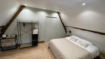 Une chambre avec un plafond en pente, un lit recouvert d’une courtepointe blanche, une table de chevet avec une lampe, une armoire et un plancher en bois.
