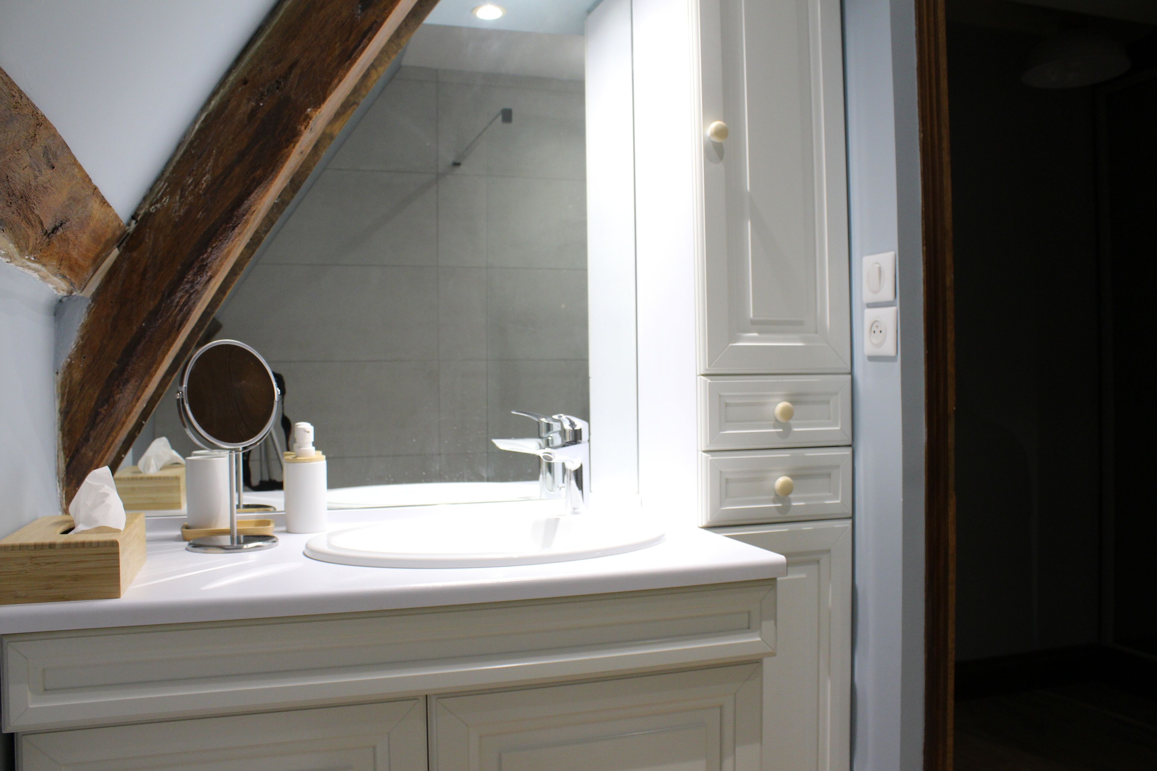 A bathroom with a white vanity, a round mirror, a sink, and a shower visible through a glass door.