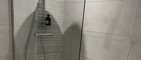 A glass-enclosed shower with a handheld showerhead, a bottle of shampoo, and a towel rack.