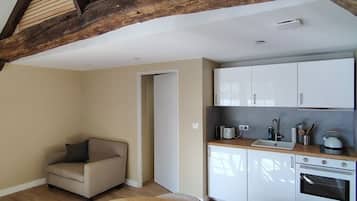Una habitación con una mesa de comedor de madera, un sofá, una cocina con armarios blancos y vigas de madera a la vista en el techo.