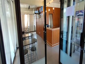 A modern hotel room with a wooden reception desk, a dining area with a table and chairs, and a large window with curtains. - OYO 1062 Casa Edna Microtel And Function (Digos City)