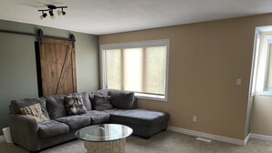 A living room with a sectional sofa, a glass coffee table, a barn-style door, and a large window. - 5 Bedroom Waterfront Lake House  (Bonfield)