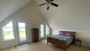A bedroom with a sloped ceiling, a bed, a nightstand, and a door leading to a balcony. - 5 Bedroom Waterfront Lake House  (Bonfield)
