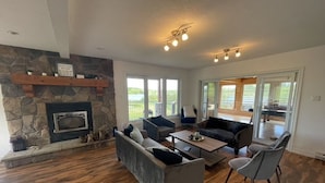A spacious living room with a stone fireplace, large windows, and a view of the outdoors. - 5 Bedroom Waterfront Lake House  (Bonfield)