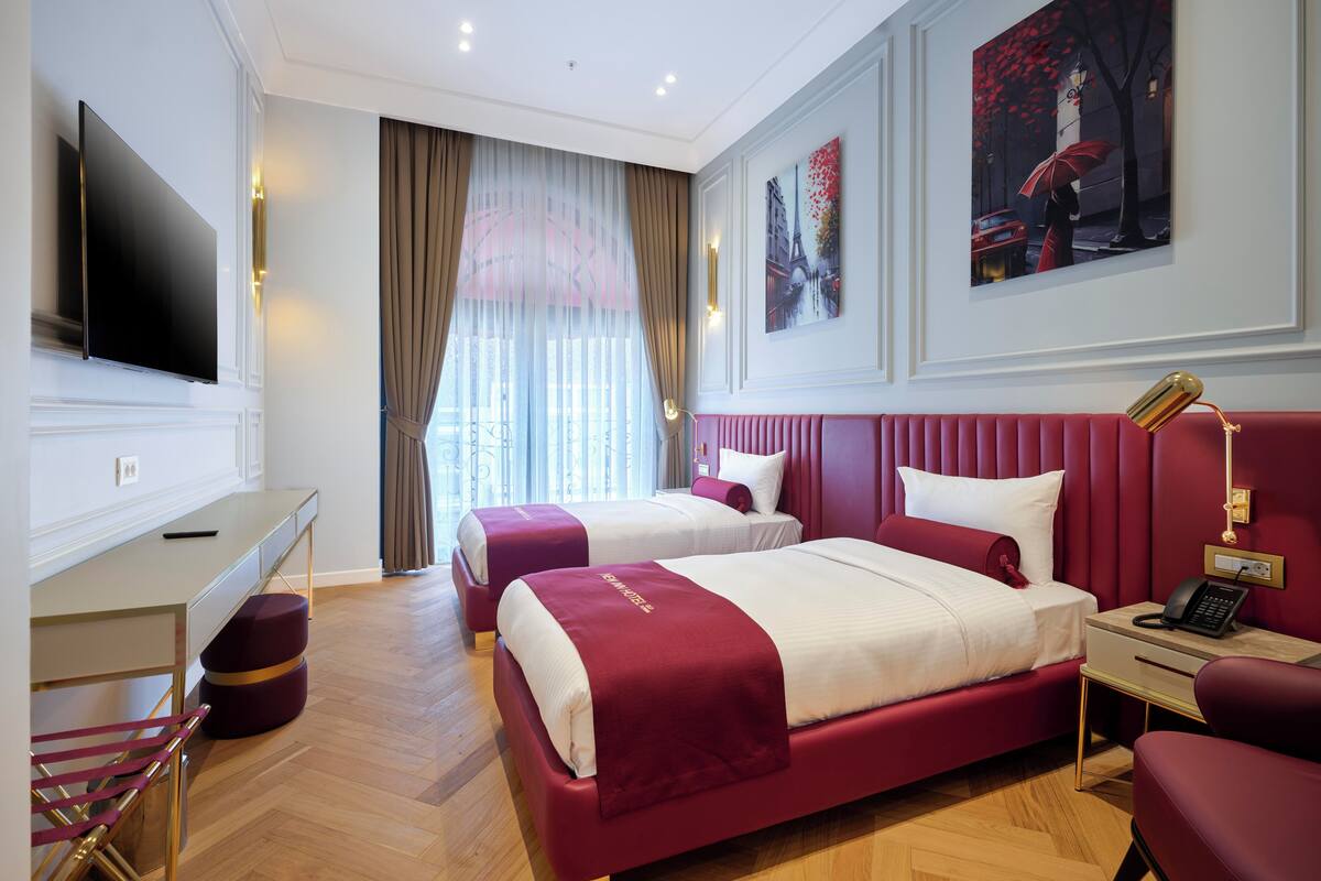 A hotel room with two beds, a desk, a TV, and artwork on the walls.
