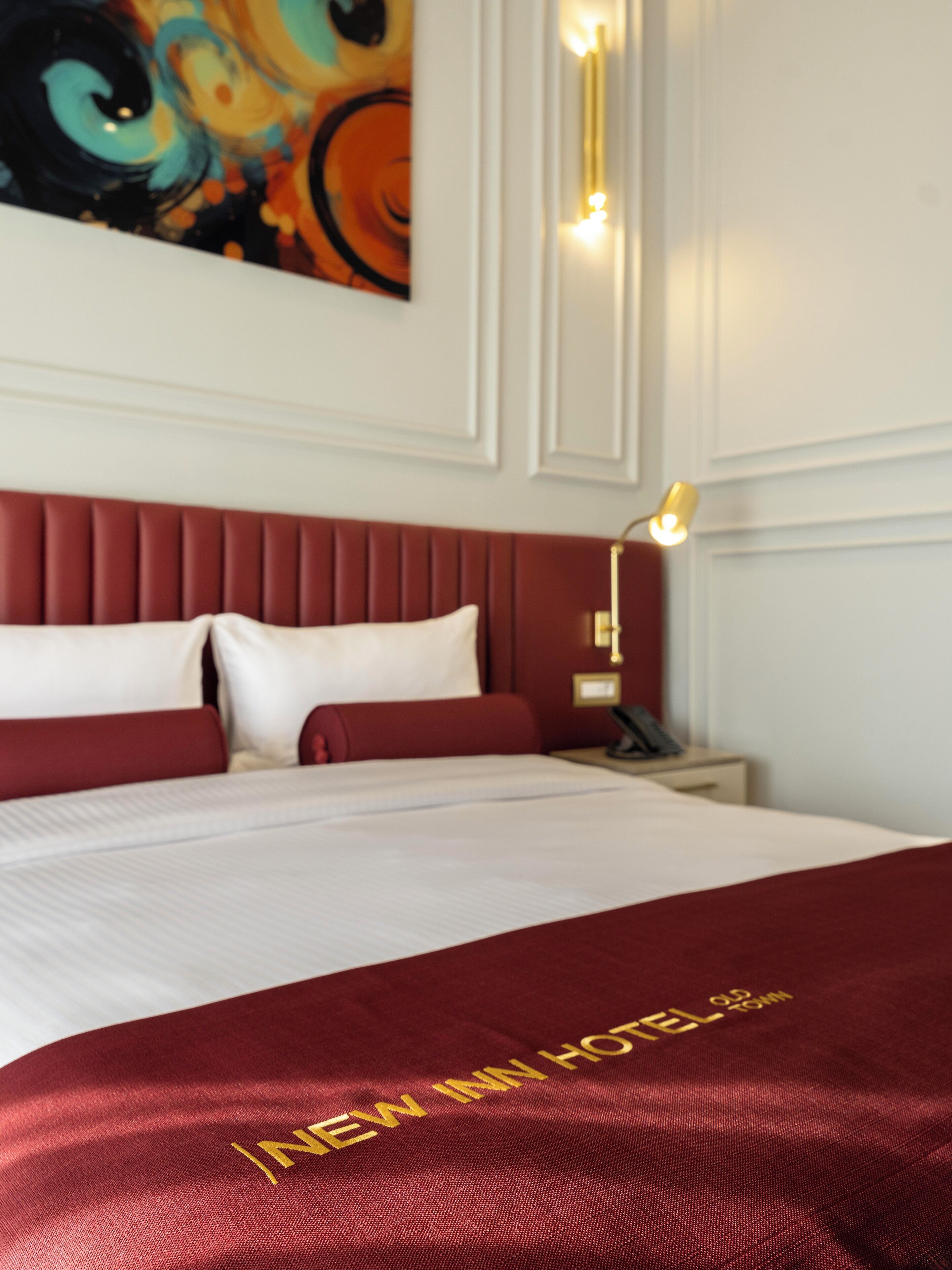 Een hotelkamer met een groot bed, een rood hoofdeinde en een schilderij aan de muur.