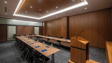 Een vergaderzaal met een lange tafel, stoelen, een spreekgestoelte en een plafond met inbouwverlichting.