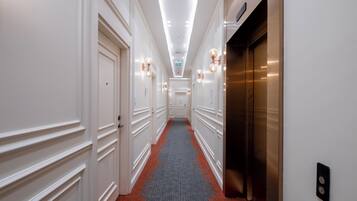 A hotel hallway with white walls, a red carpet, and an elevator on the right.
