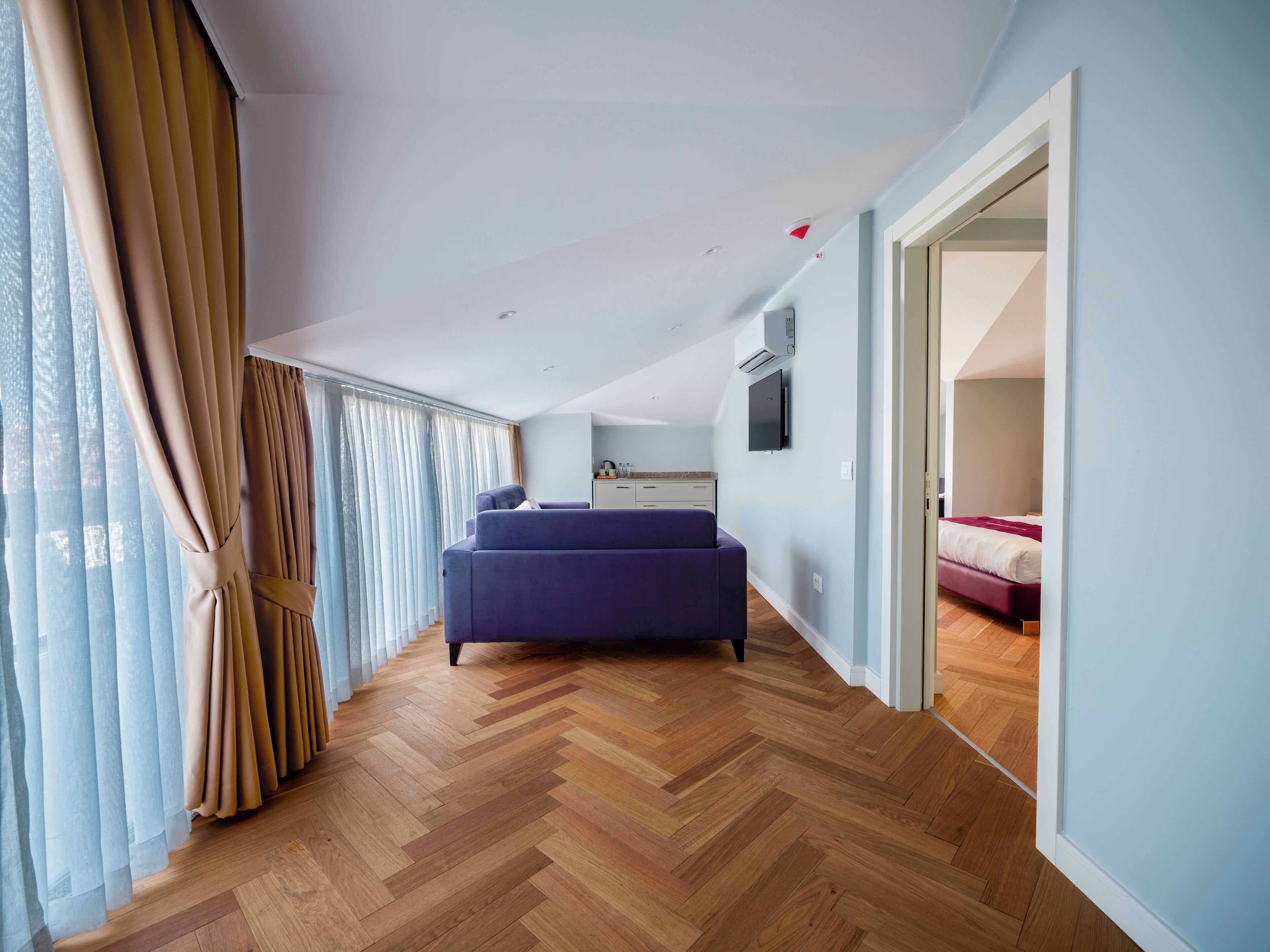 Quarto moderno com uma cama grande, uma kitchenette e vista pela janela com cortinas.
