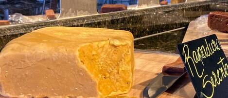 Un gran bloc de formatge sobre una taula de fusta amb un ganivet i un cartell que diu 'Ramblesure Cheese'.