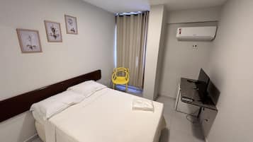 Una camera d'albergo con un letto, una sedia, una scrivania con un computer e un condizionatore d'aria.