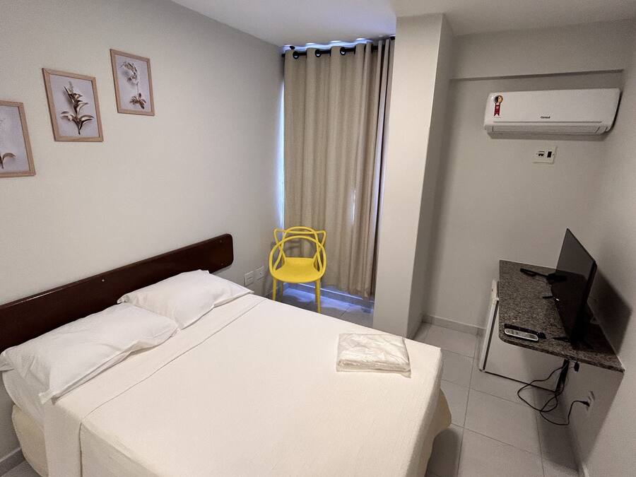 Una camera d'albergo con un letto, una sedia, una scrivania con un computer e un condizionatore d'aria.