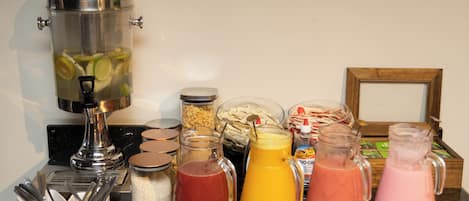 A breakfast bar with various food items and beverages, including a coffee maker, jars of granola, and pitchers of fruit juices.