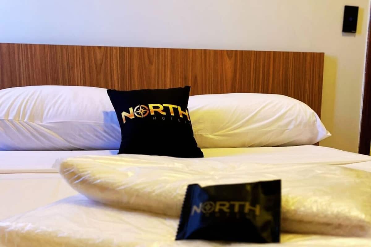 Ein Hotelbett mit Holzkopfstütze, zwei Kissen mit dem Hotel-Logo und einer Decke mit dem Logo.