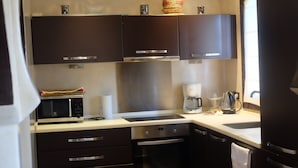 A compact kitchen with dark cabinets, a microwave, an oven, a coffee maker, and a sink. - Eden Palm Resident Marrakech (Marrakech)