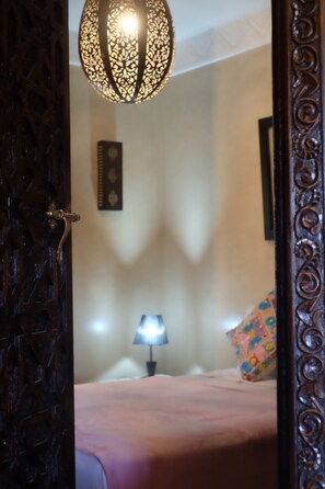Quarto com cama, mesa de cabeceira, luminária e um enfeite de parede.