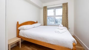 Ein Einzelbett mit Holz Kopfteil, weißer Bettwäsche und einem kleinen Nachttisch.