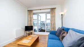 Ein modernes Wohnzimmer mit einem blauen Sofa, einem Holztisch und einem Fernseher auf einem Lowboard.