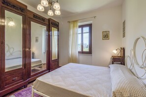 A bedroom with a large bed, a wardrobe, a window with curtains, and a bedside table with a lamp.