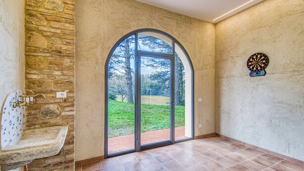 Une pièce avec un mur en pierre, une grande fenêtre en arc de cercle, un jeu de fléchettes et un lavabo.