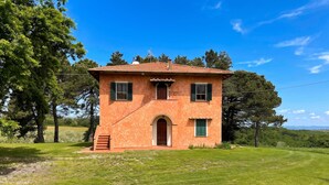 Une maison à deux étages, avec un toit recouvert de tuiles rouges, une porte d’entrée centrale en arc de cercle et un petit porche.