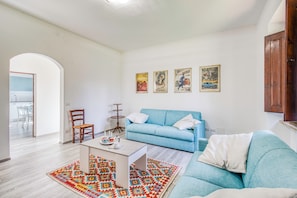 Uma sala de estar com um sofá azul, uma mesa de centro e um tapete estampado. Há três quadros na parede.