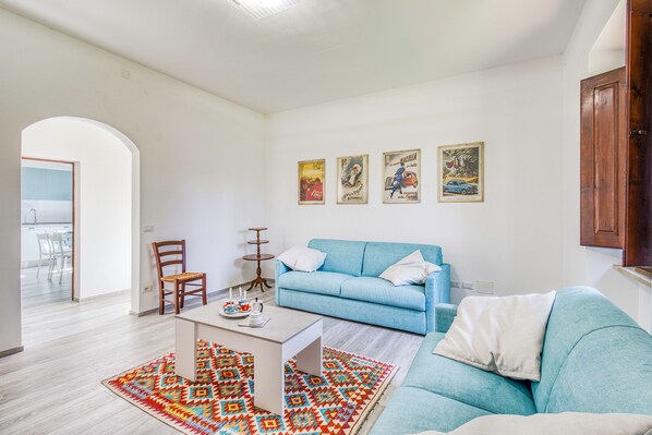 Un salon avec un canapé bleu, une table basse, un tapis à motifs et trois affiches accrochées au mur.