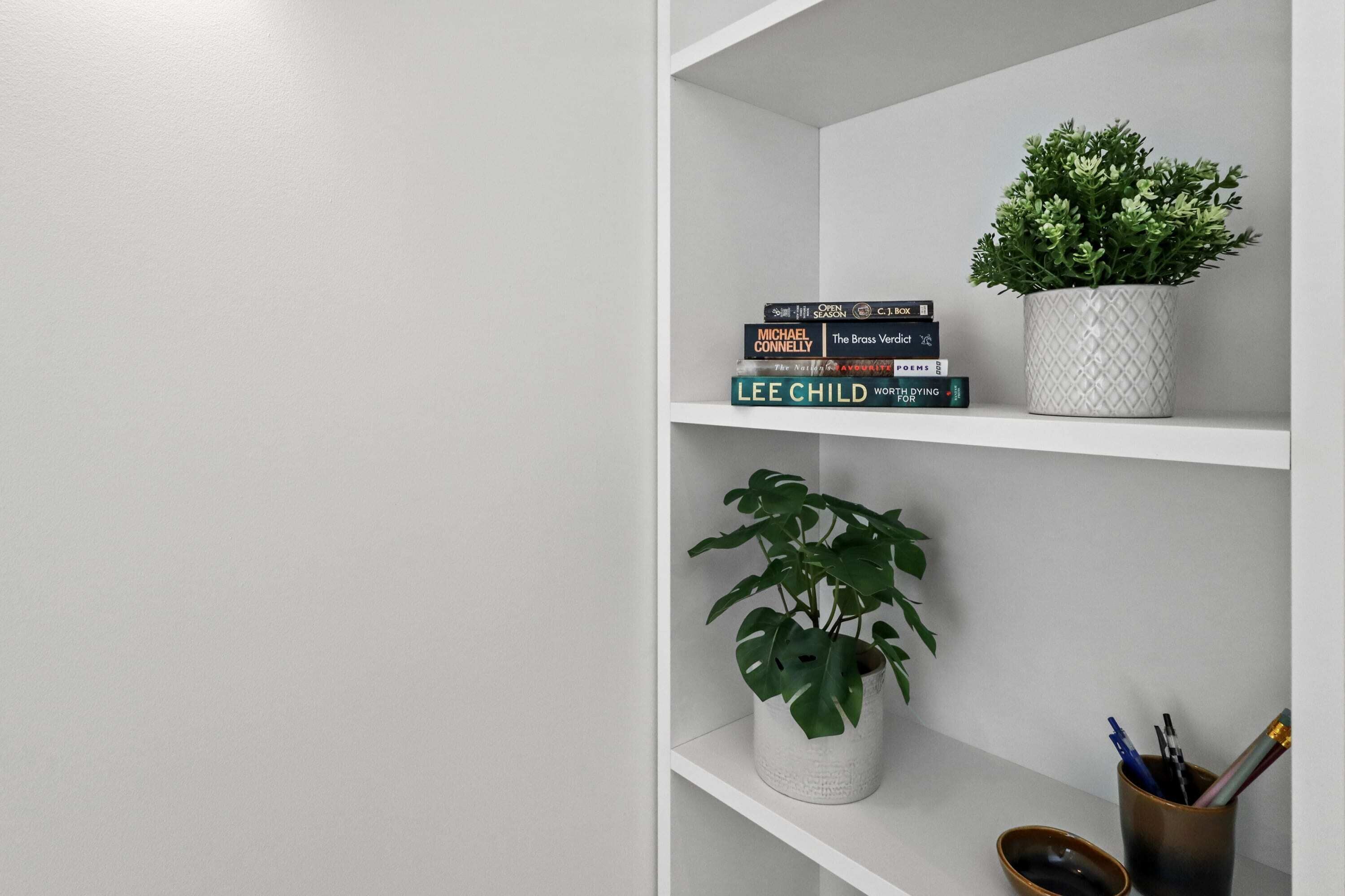 A bookshelf with books and two potted plants.