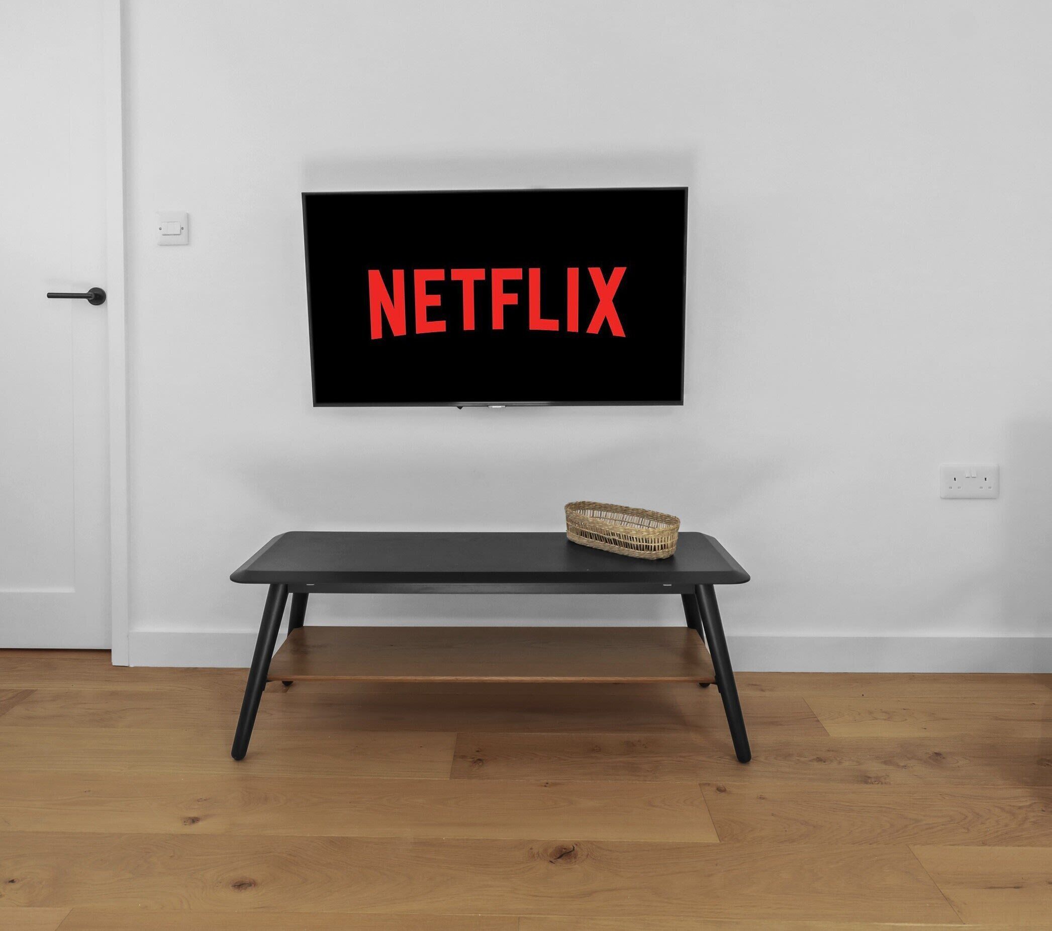 Une pièce avec un téléviseur fixé au mur blanc, un banc en bois et un panier en osier posé sur le banc.