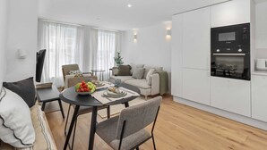 A modern living room with a dining area, a sofa, a coffee table with fruit, and a built-in oven. - Escape to Luxury Stylish Apartment in Eastbourne (Eastbourne)