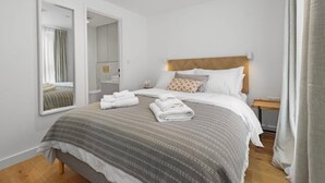 Une chambre d’hôtel moderne avec un grand lit, une tête de lit en bois, une table de chevet avec une lampe et un miroir.
