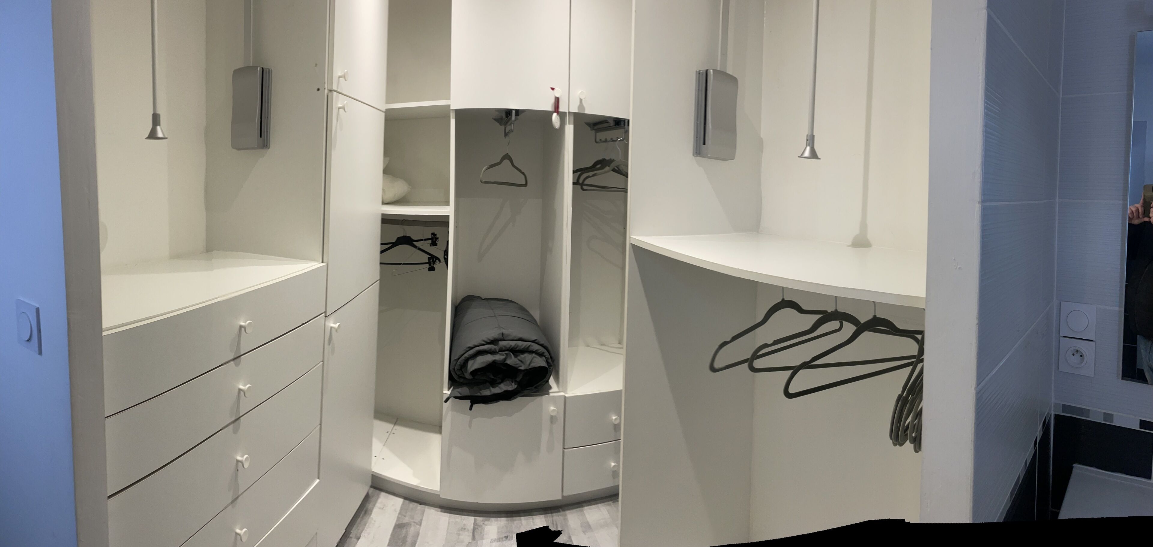 A walk-in closet with open doors, featuring multiple shelves, hanging space, and a folded blanket.